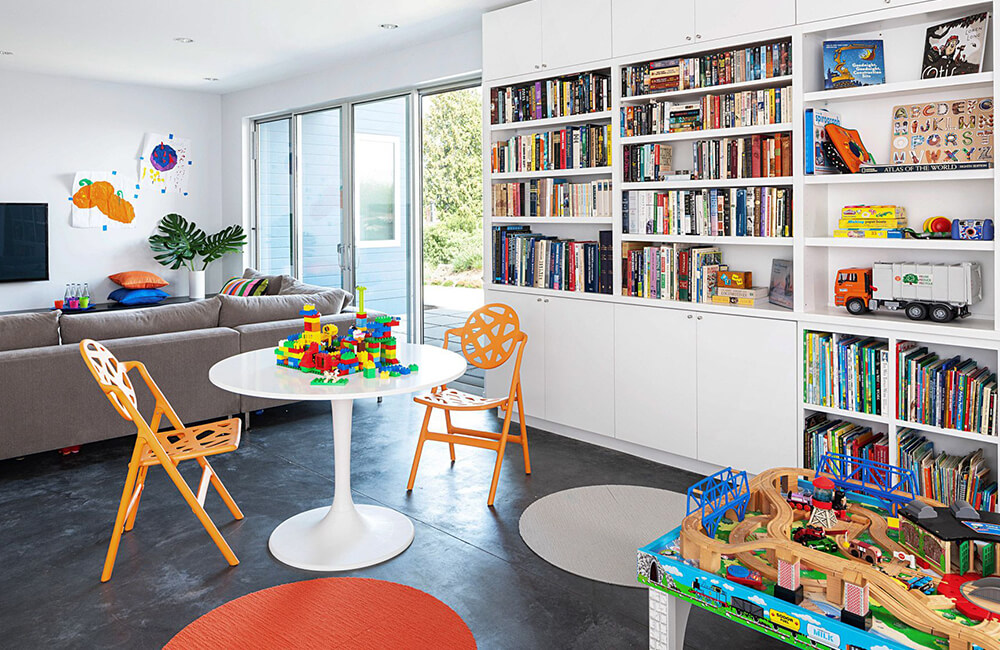 there is a many books on wall book shelf with kids toy's also there is a white stool with two chairs