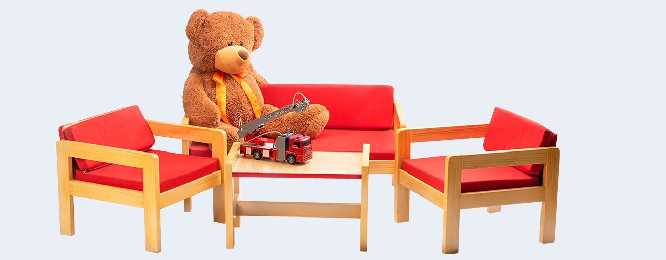a teddy bear sitting on a couch with a toy fire truck on the table