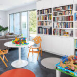 there is a many books on wall book shelf with kids toy's also there is a white stool with two chairs
